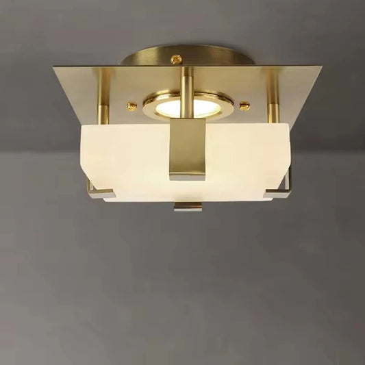 Close-up of a square gold flush mount ceiling light with a frosted glass shade and geometric brass details.