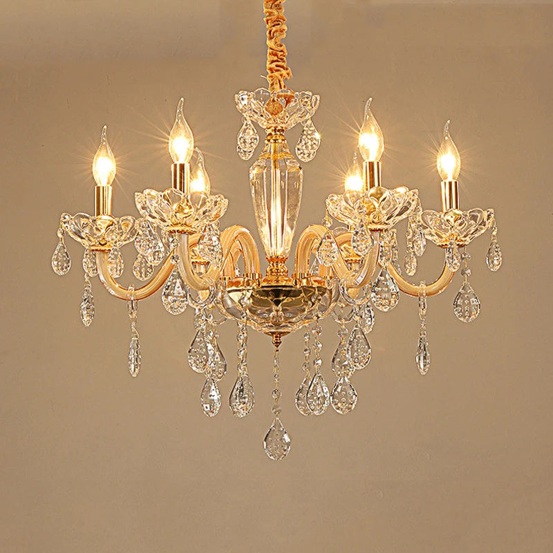 Close-up of a gold crystal chandelier with multiple arms and dangling crystals, illuminated against a plain background.