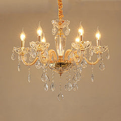 Close-up of a gold crystal chandelier with multiple arms and dangling crystals, illuminated against a plain background.