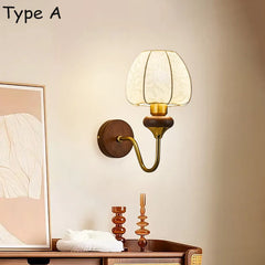 Wall sconce with a round wooden base, a curved brass arm, and a bell-shaped glass shade in a room setting.