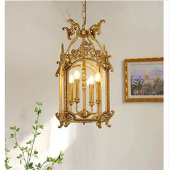 A gold candelabra-style pendant light with a decorative cage frame, hanging in a well-lit room with a painting on the wall.