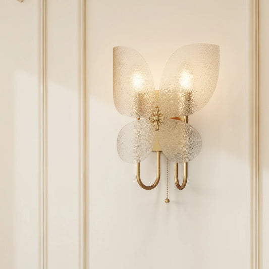 Gold butterfly-shaped wall sconce with frosted glass shades mounted on a white paneled wall, casting soft shadows.
