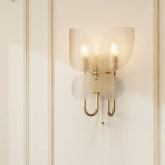Gold butterfly-shaped wall sconce with frosted glass shades mounted on a white paneled wall, casting soft shadows.