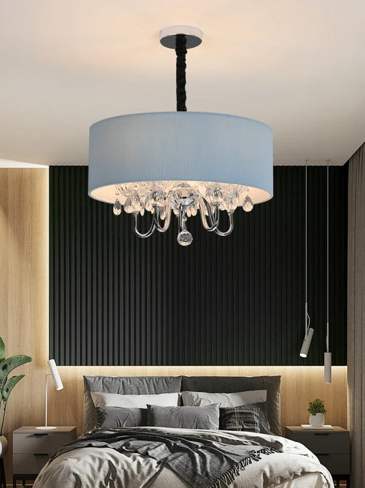 Blue fabric drum pendant light with cascading crystal accents hanging over a bed.