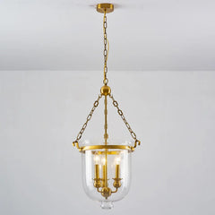 Polished copper and clear glass drum pendant light hanging from a chain against a white ceiling