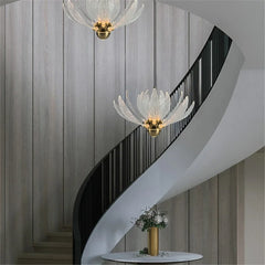Two clear acrylic lotus flower pendant lights hanging near a curved staircase with wooden walls and a black railing.