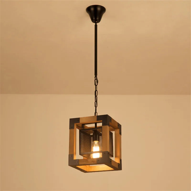 Square industrial pendant light with wood frame and dark metal cage, featuring one exposed bulb suspended by a chain from a ceiling canopy.