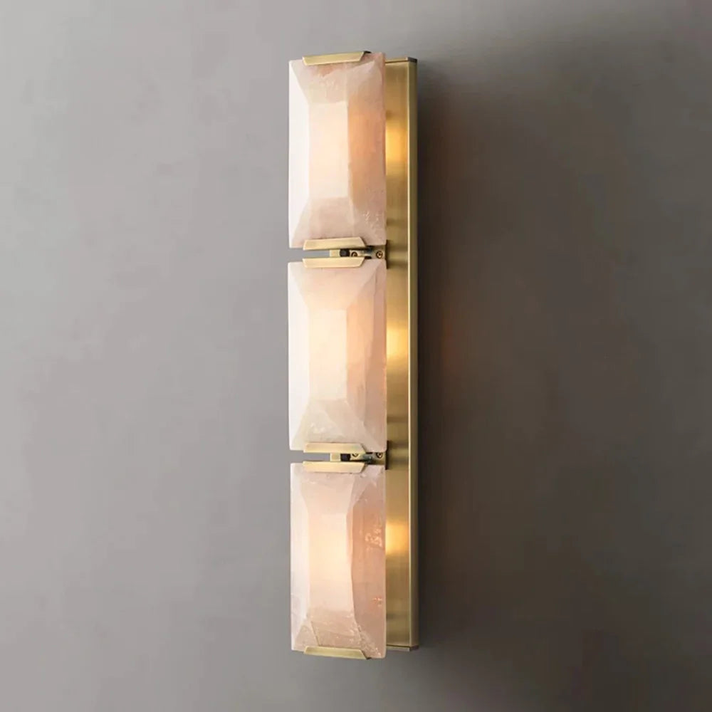 Wall-mounted light fixture with gold frame and glass shades on a gray wall.