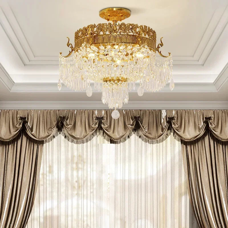 View of a gold semi-flush crystal ceiling light above a window with luxurious brown drapes and sheer curtains.