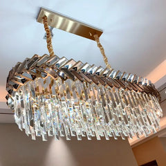 An angled view of a gold rectangular-shaped chandelier featuring layered clear crystals and a semi-flush mount, suitable for modern interiors.