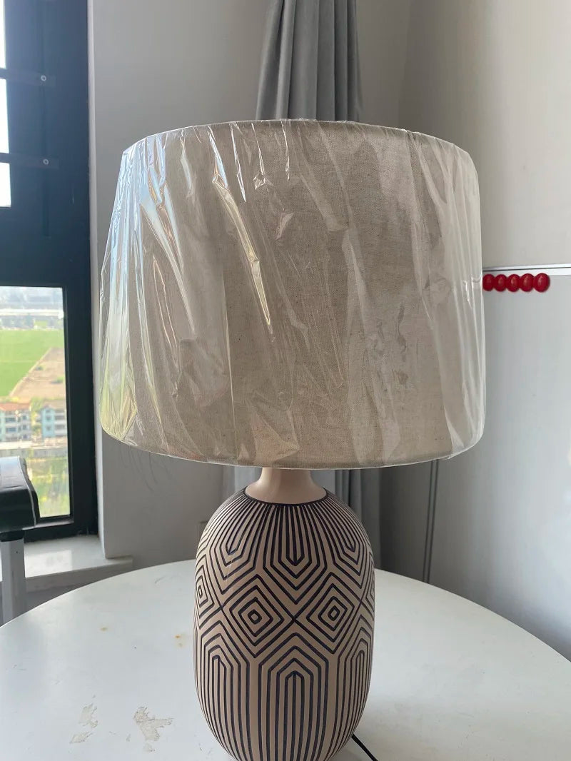 Table lamp with a patterned base and beige shade on a surface.