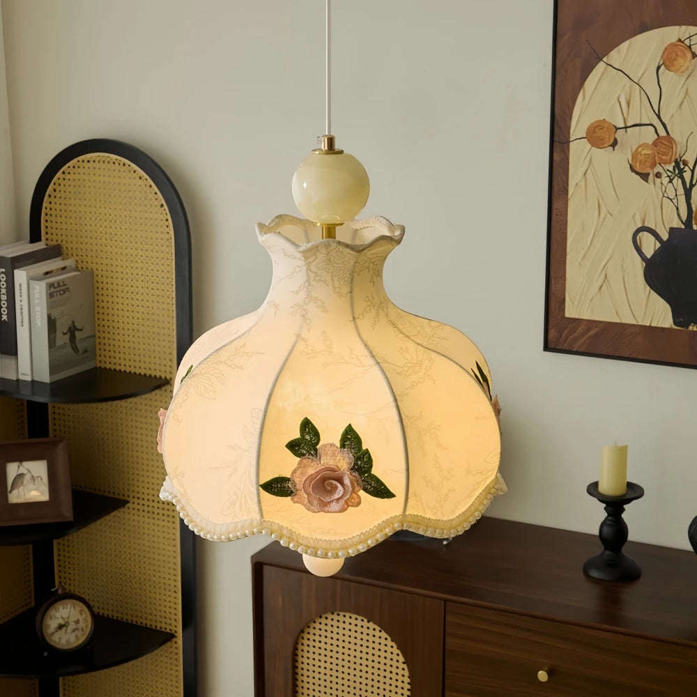 Champagne fabric pendant light with floral rose embroidery and beaded trim hanging in a room with wooden furniture.