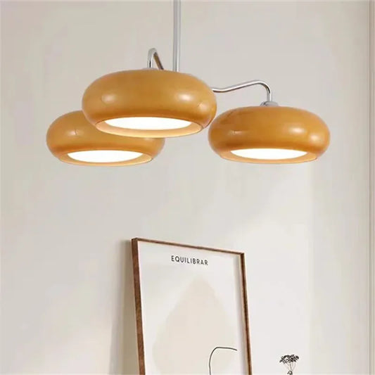 Three yellow glass dome shades on a chrome multi-arm chandelier against a white wall