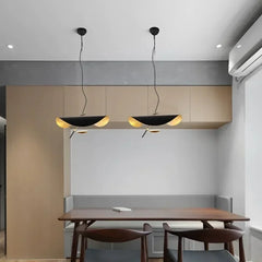 Two black and gold leaf wave pendant lights hanging above a wooden dining table in a contemporary setting.