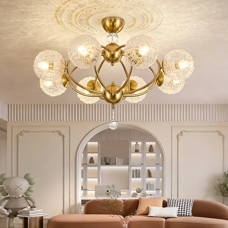 A polished gold chandelier with globe crystal shades is shown in an arched doorway, leading to a living area with a sectional sofa and decorative elements.
