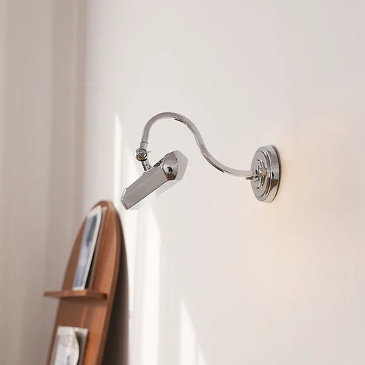 Close-up of a polished chrome wall sconce, showing the adjustable joint and the angled light head.