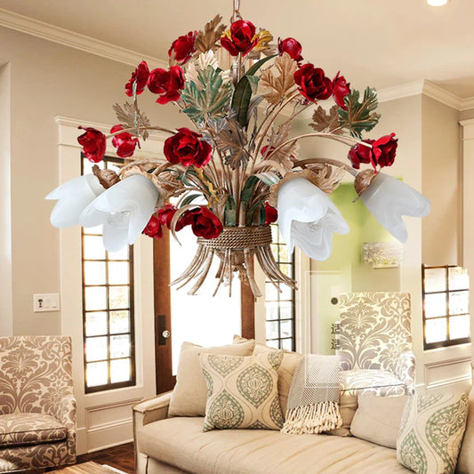 A gold floral pendant light with red rose buds and white glass shades, hanging above a light-colored sofa and chairs in a living room setting.