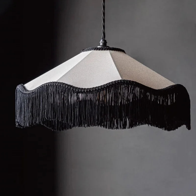 Close-up of a black and white fabric pendant light featuring a scalloped shade with dramatic black tassels against a dark background.