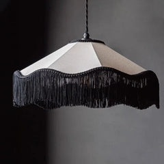 Close-up of a black and white fabric pendant light featuring a scalloped shade with dramatic black tassels against a dark background.