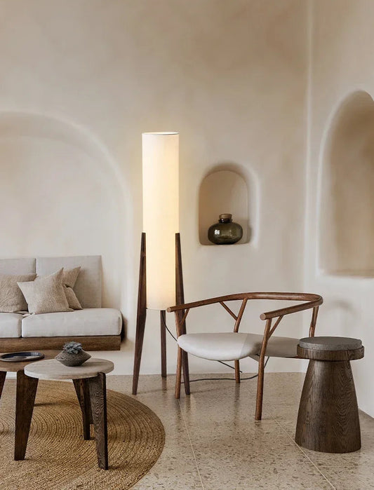 A floor lamp with a black walnut base and a white fabric shade, casting a warm glow in a bright, airy room with natural textures and arched wall details.