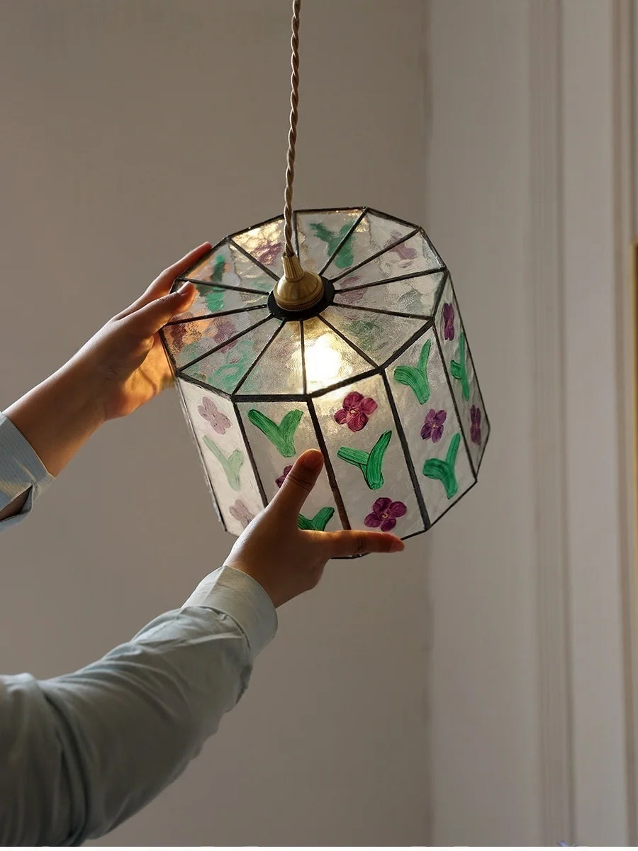 Hand holding a stained glass lamp with floral designs against a neutral background