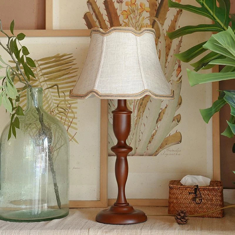 Wooden table lamp with a white lampshade on a surface with decorative elements.