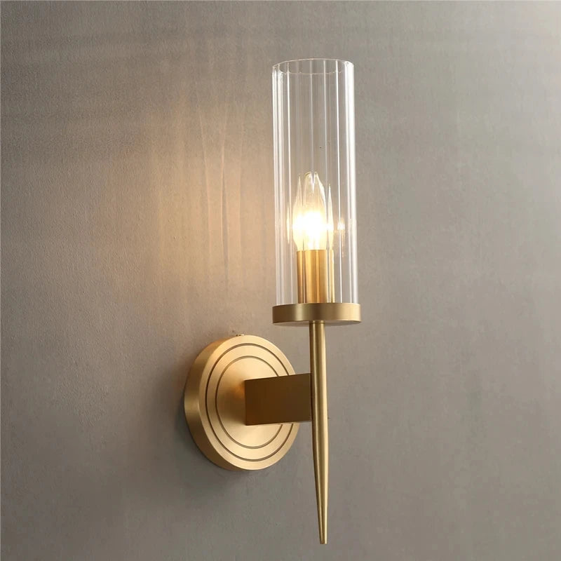 Gold wall sconce with clear glass shade on a gray wall
