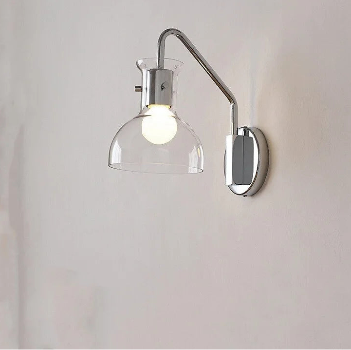 Close-up of a polished chrome wall sconce with a clear glass dome shade and a metal arm against a white background.