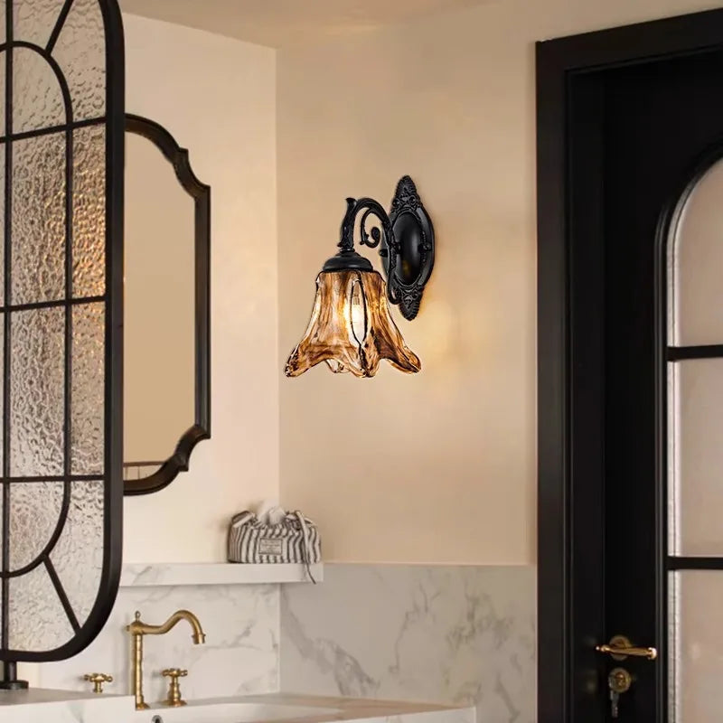 A bronze glass bell wall sconce mounted on a wall above a marble countertop, near a black door.