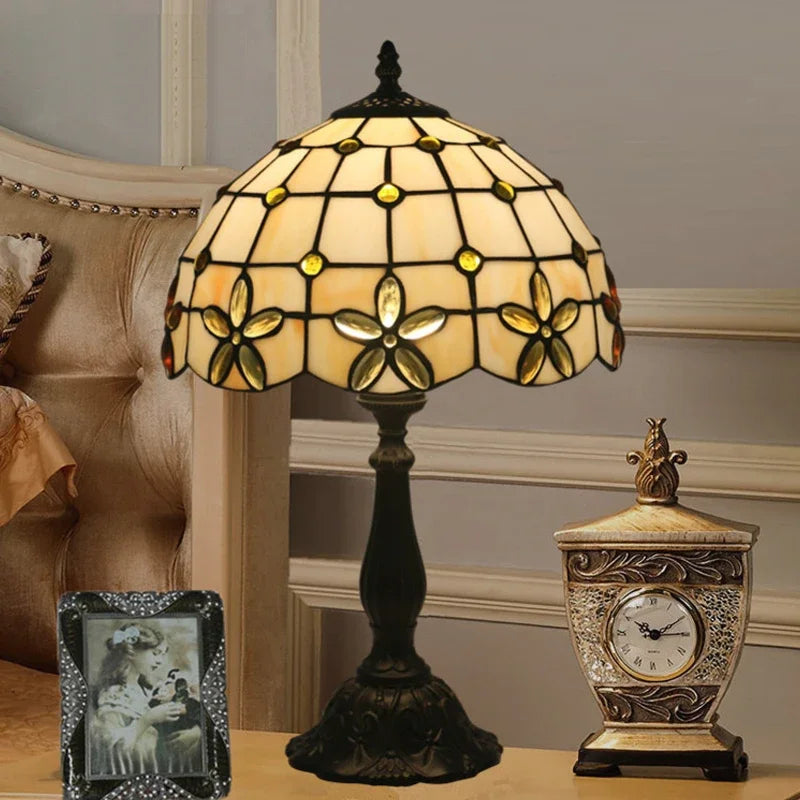 Tiffany stained glass floral table lamp on a nightstand next to a bed and clock.