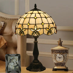 Tiffany stained glass floral table lamp on a nightstand next to a bed and clock.