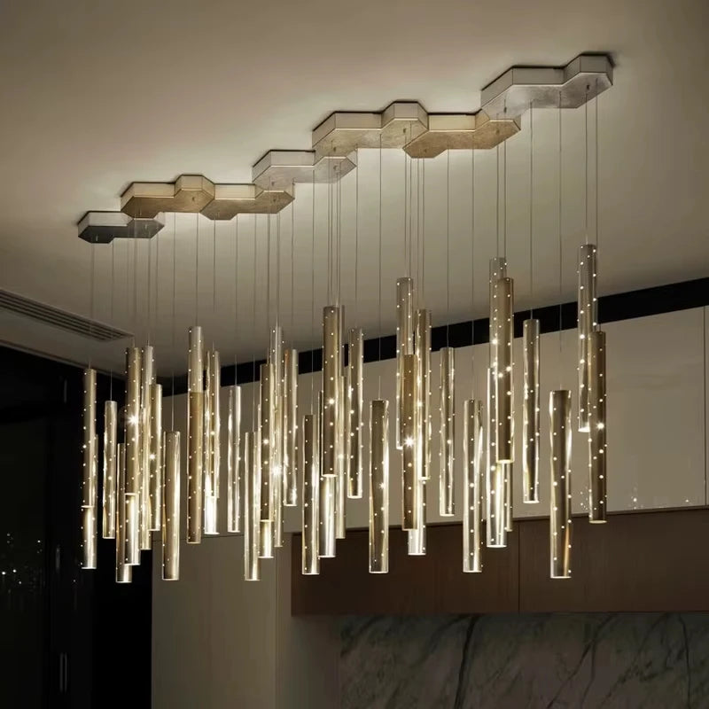 Close-up view of a modern chandelier with numerous hanging gold and silver tubes, each containing small lights, attached to a multi-faceted hexagonal ceiling canopy.