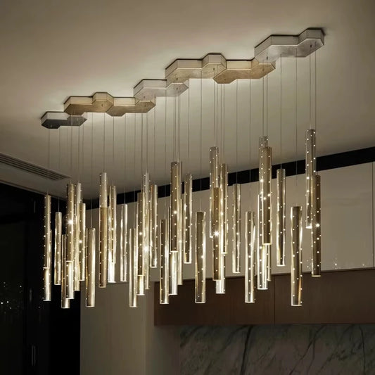 Close-up view of a modern chandelier with numerous hanging gold and silver tubes, each containing small lights, attached to a multi-faceted hexagonal ceiling canopy.
