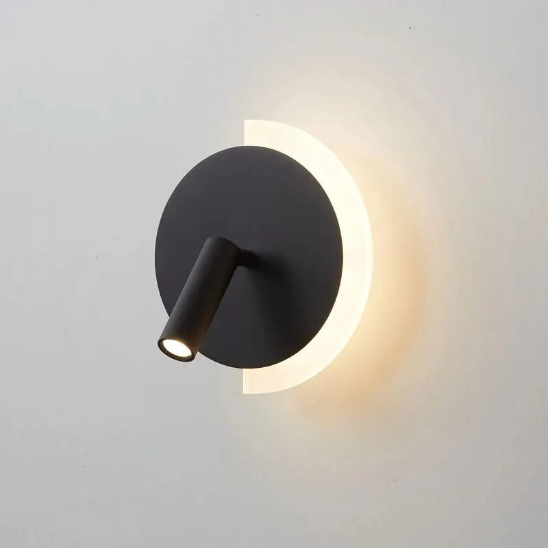 Black modern LED wall lamp with a circular backplate and adjustable spotlight, emitting warm light against a white wall.