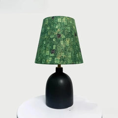 Black ceramic table lamp with a textured green fabric shade featuring a subtle geometric pattern, on a white surface.