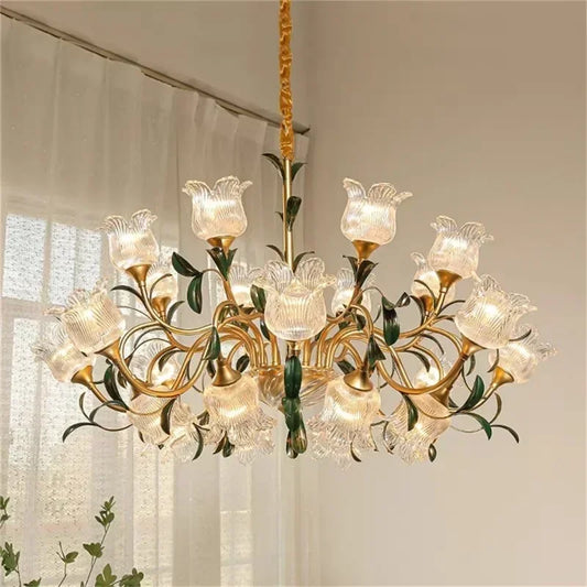 Wide shot of a multi-arm gold chandelier with clear glass floral shades, installed in a softly lit room with curtains in the background.