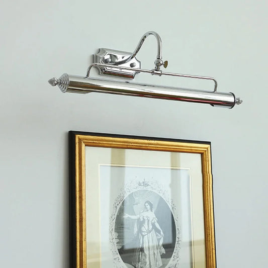 A silver-colored linear wall sconce with an adjustable arm and shade is mounted on a white wall above a framed picture.