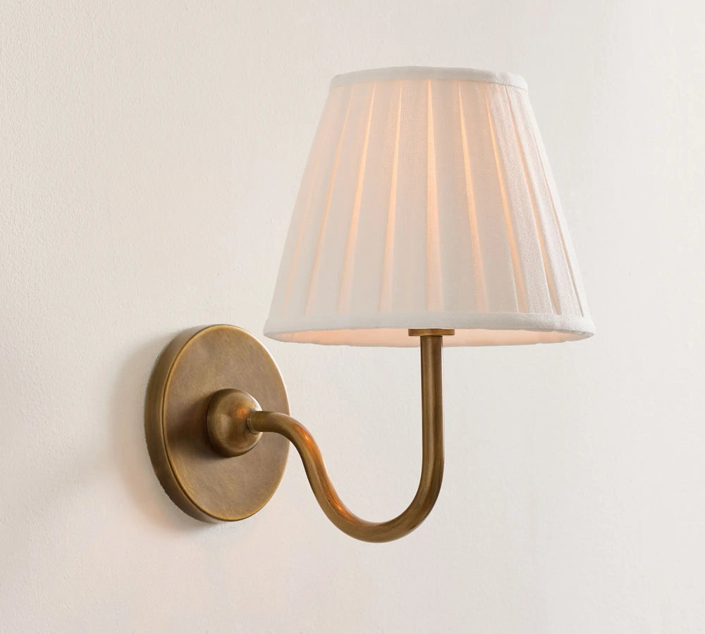 Wall-mounted lamp with a white pleated shade and brass arm on a light gray background