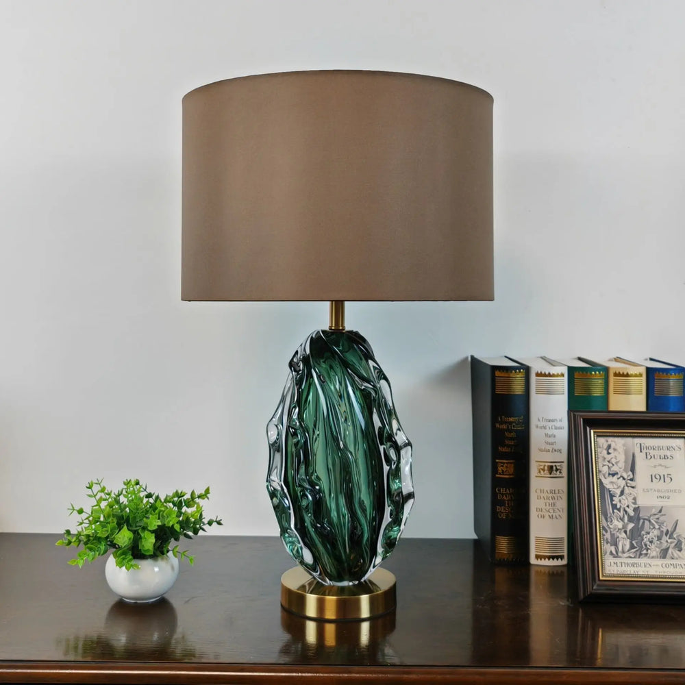 Decorative table lamp with a green base and brown shade on a wooden surface.