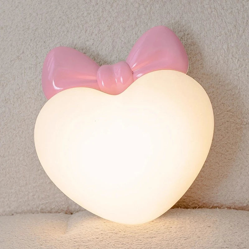 Close-up of a pink bow heart-shaped wall sconce with a warm glow.