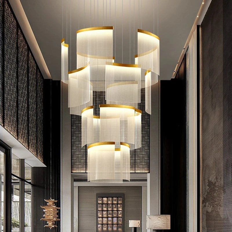 A large gold cascading crystal chandelier hanging in a grand foyer with a double staircase.