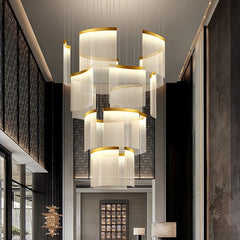 A large gold cascading crystal chandelier hanging in a grand foyer with a double staircase.