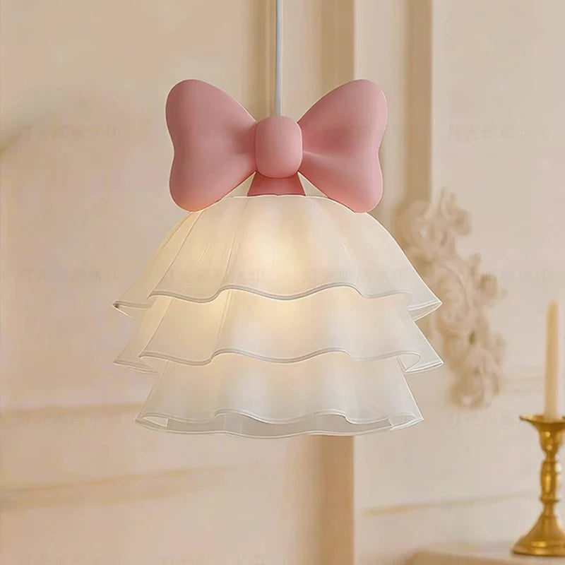 Side view of a white tiered chandelier with a prominent pink bow accent, illuminated.