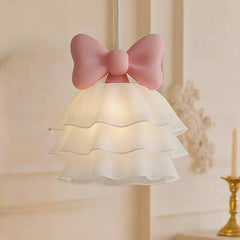 Side view of a white tiered chandelier with a prominent pink bow accent, illuminated.
