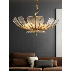 A gold leaf floral chandelier with clear glass petals displayed above a brown sofa.