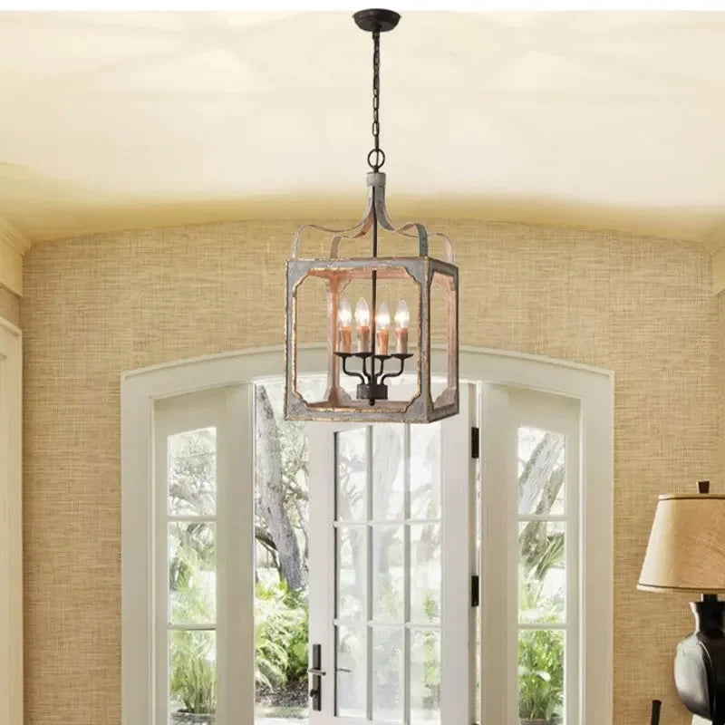 Distressed gray and gold lantern chandelier installed in a room above double doors, with light filtering through.