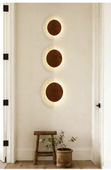 A vertical arrangement of three modern crescent-shaped wall sconces with wood circles and speckled stone arcs in a hallway.