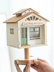 Hands holding a white tree house table lamp, showcasing its intricate wooden construction and artful design.