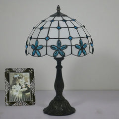 Blue Tiffany stained glass floral table lamp with a dark base, shown with a framed photo.