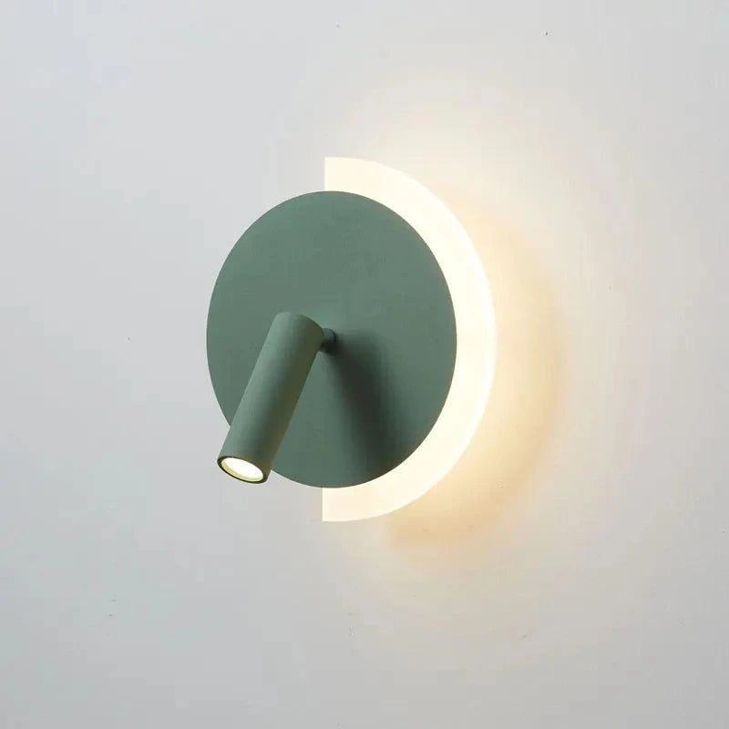 Green modern LED wall lamp with a circular backplate and adjustable spotlight, emitting warm light against a white wall.